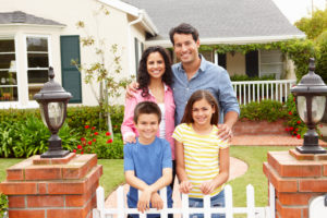 Hispanic family of four standing in front of their new home built buy custom home builders