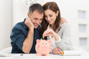 middle aged couple putting a coin into a piggy bank implying the saving of money