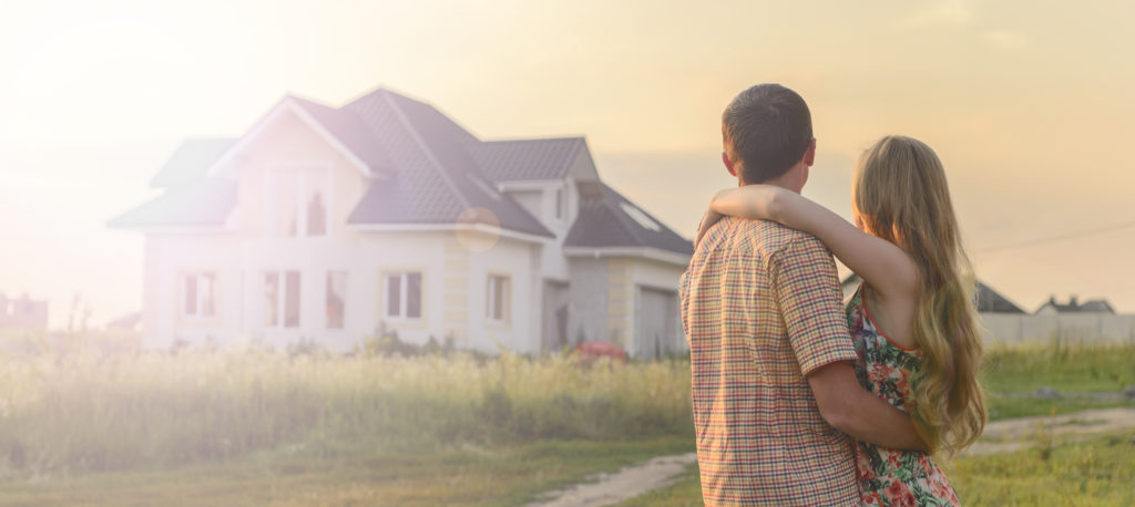 a couple of home buyers embraced in a loving hug looking on at a new home