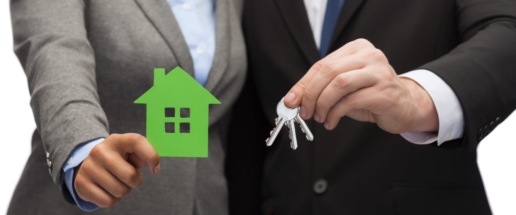 a real estate agent holding keys and handing them to a person who is buying a new home and holding a green cutout of a simple house