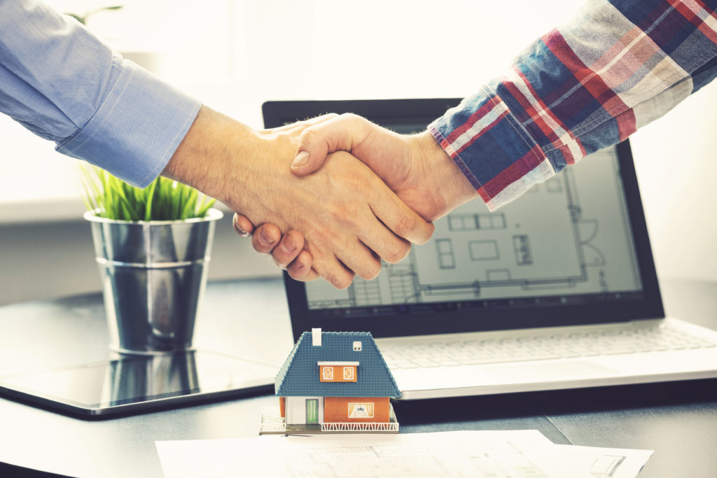 men shaking hands above a toy model home after buying a home