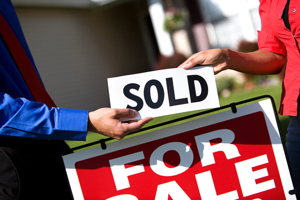 a realtor's hand handing over a sold sign to a buyer's hand over a for sale sign