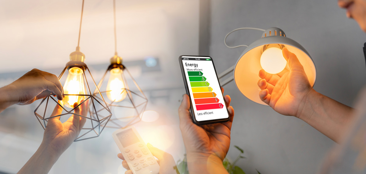Two people installing new light bulbs while looking at their energy efficiency rating on a smartphone in El Paso.