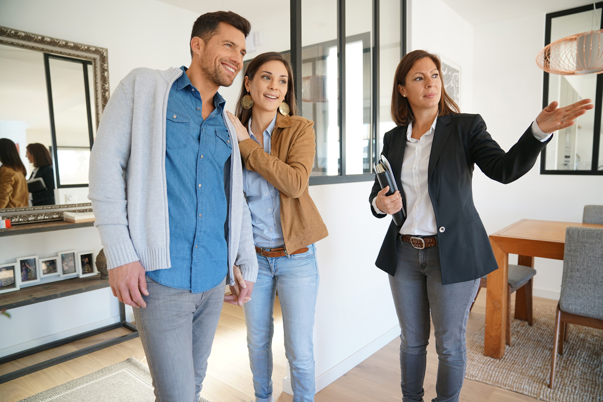 A smiling couple with a real estate agent touring a new home in El Paso.